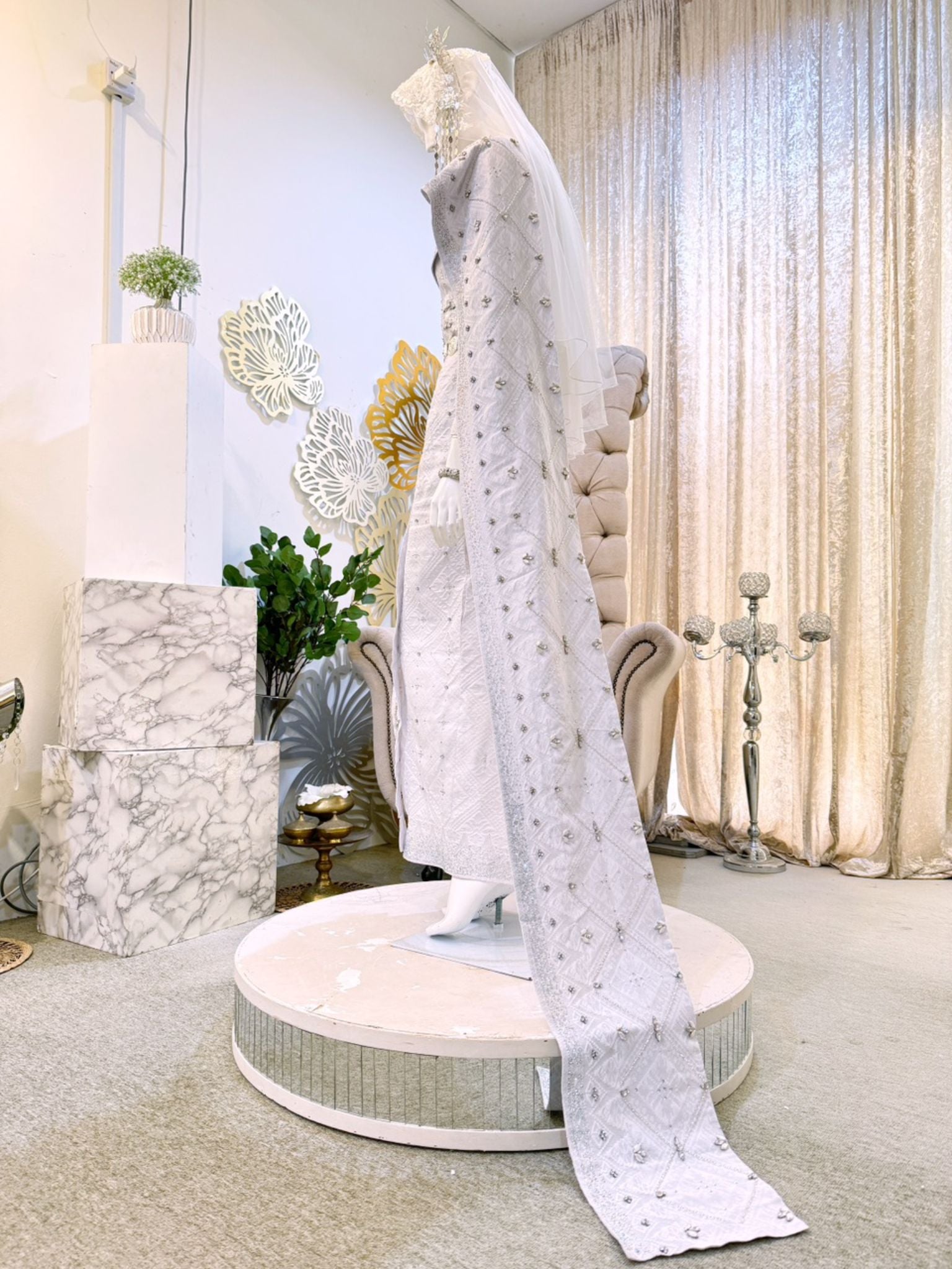A photograph showcasing Nilam Sari's Baju Pengantin Songket in White with Silver, a blend of Thai-inspired bridal attire. The image captures the bride's ensemble, featuring a graceful Thai Dress design crafted from luxurious Songket 2D material, and the groom's attire, adorned with the intricate Kot Raihan 2pcs