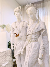 A photograph showcasing Nilam Sari's Baju Pengantin Songket in White with Silver, a blend of Thai-inspired bridal attire. The image captures the bride's ensemble, featuring a graceful Thai Dress design crafted from luxurious Songket 2D material, and the groom's attire, adorned with the intricate Kot Raihan 2pcs