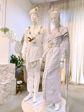 A photograph showcasing Nilam Sari's Baju Pengantin Songket in White with Silver, a blend of Thai-inspired bridal attire. The image captures the bride's ensemble, featuring a graceful Thai Dress design crafted from luxurious Songket 2D material, and the groom's attire, adorned with the intricate Kot Raihan 2pcs