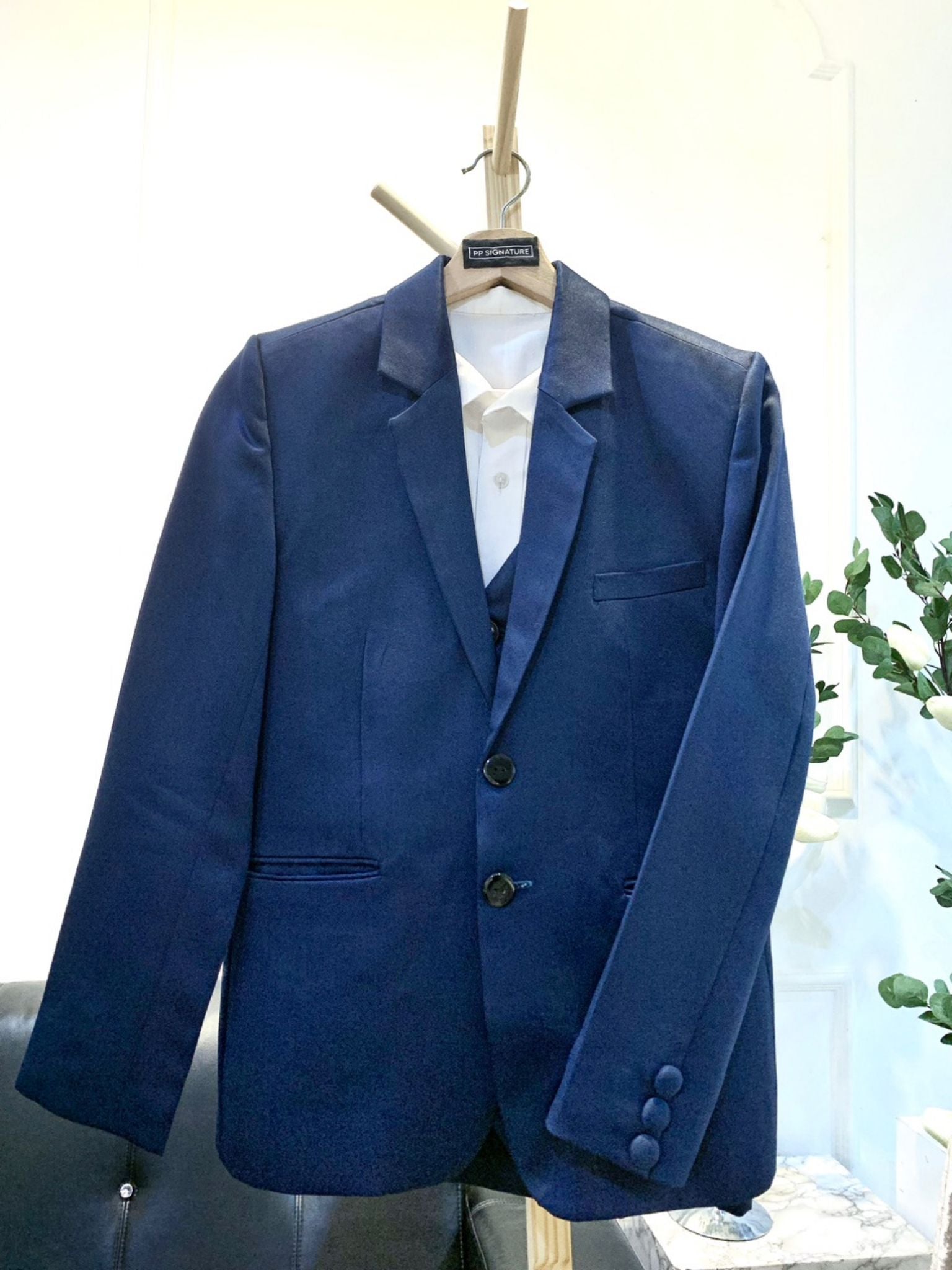 Blue suit jacket hanging on a wooden hanger. The jacket is made of a light blue fabric and has a single-breasted design with a notch lapel. It is suitable for formal occasions, such as weddings or job interviews.