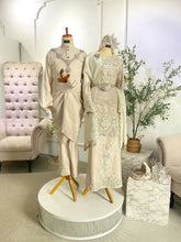 Mannequins wearing embroidered outfits in a room with a chair and plant.-Baju sanding kurung moden krim-Sewa baju pengantin warna champagne-Baju pengantin perempuan petite size